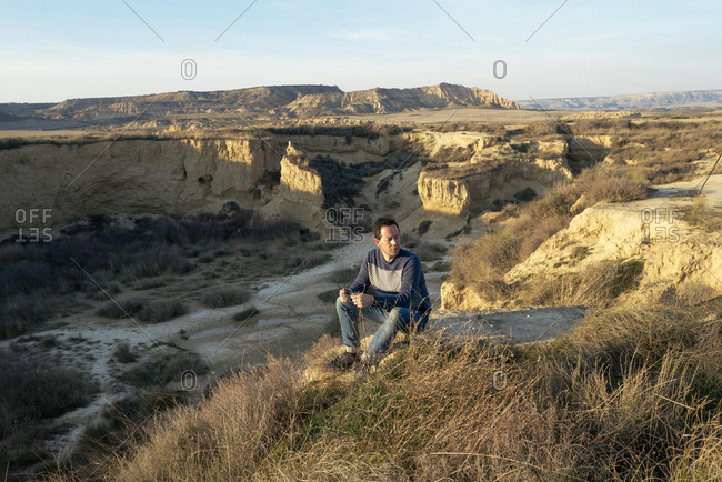 Side view of a relaxed man sitting on top of a desert canyon while looking away