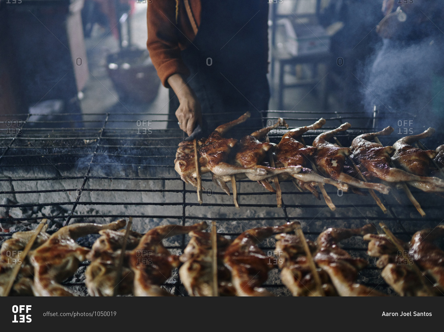 A woman grills chickens over an outdoor fire at a restaurant in Buriram, Thailand
