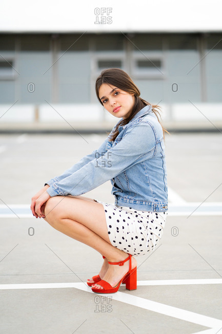 Stylish young woman wearing a light blue jean jacket and polka dot skirt with red heels