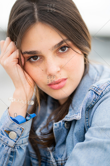 Close up portrait of a beautiful young woman wearing a light blue jean jacket with a sultry expression