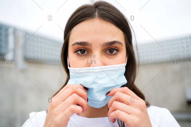 Close up portrait of young brunette woman wearing a disposable facemask looking at camera