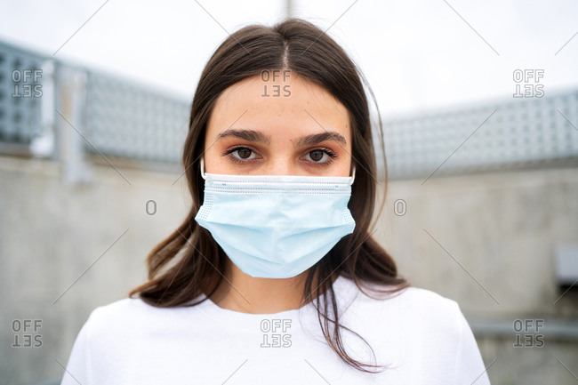 A young brunette woman wearing a disposable facemask looking at camera