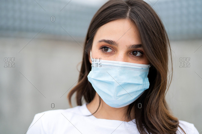 A young brunette woman wearing a disposable facemask and looking away