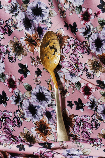 A golden spoon, with remains of vegetable soup, on a floral-patterned fabric