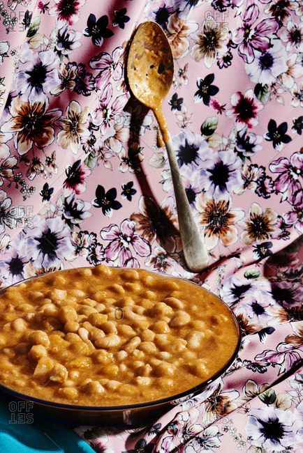 A glass plate with potaje, a Spanish traditional legume stew made with beans and chickpeas, on a floral-patterned fabric