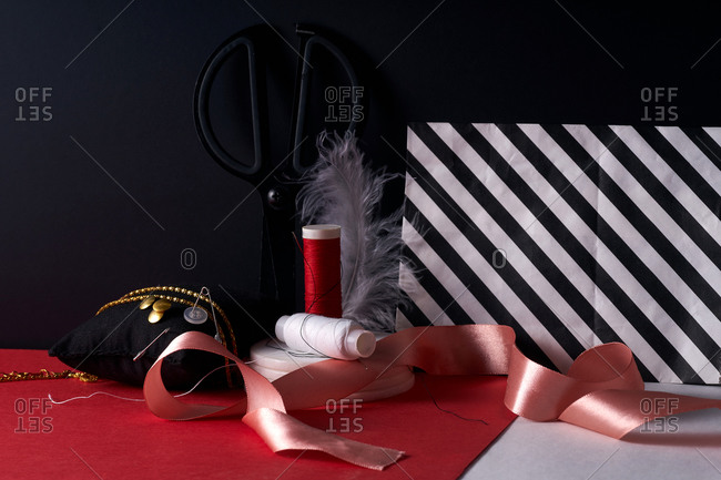 Ribbon and threads with scissors and other items on red and black background