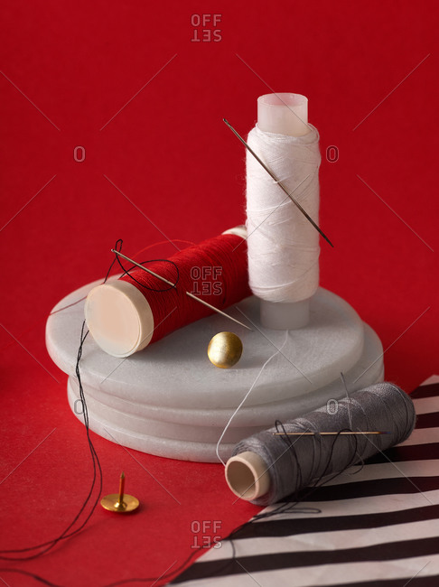 Threads and needles with thumbtacks on red background