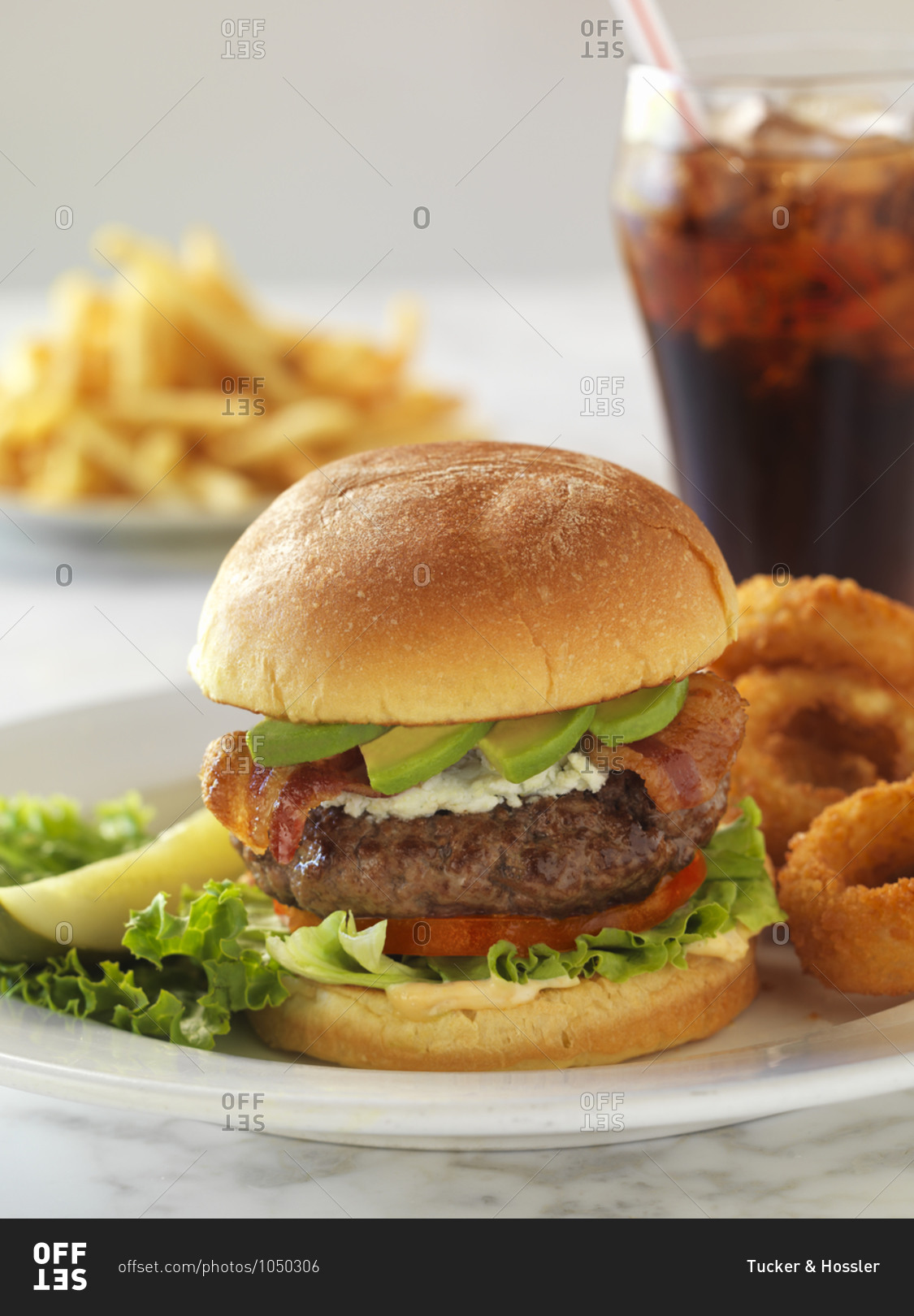 A hearty meal of a blue cheese burger with bacon a pickle, onion rings and soda.