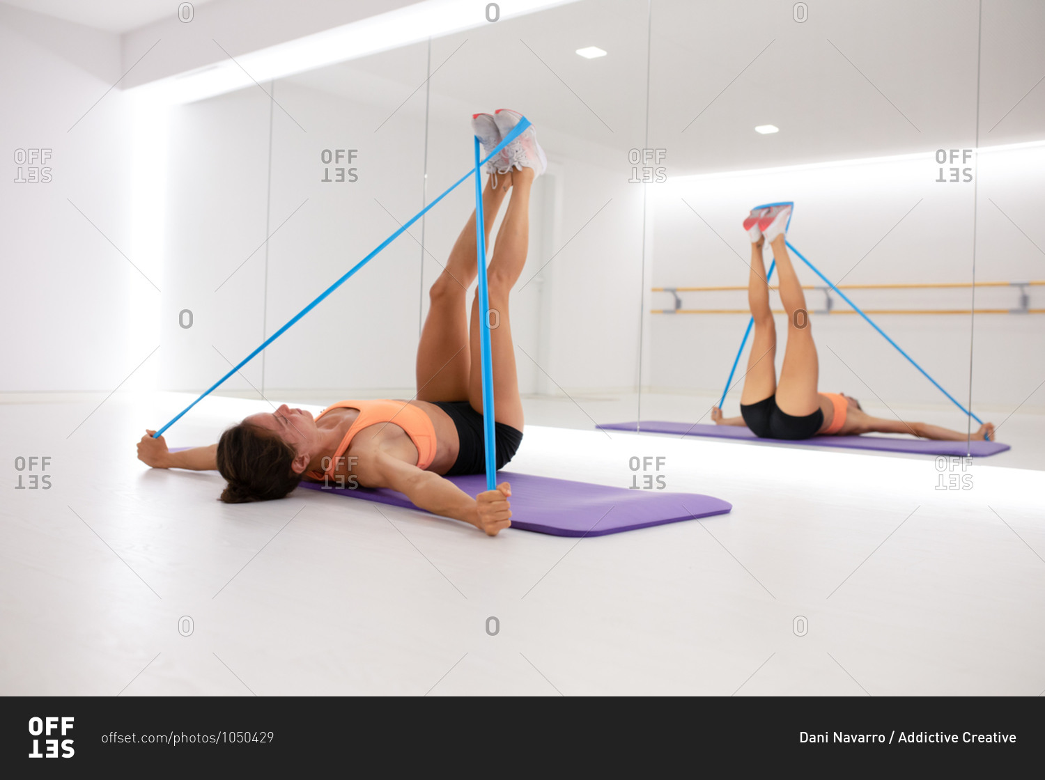 Fit female athlete stretching arms and legs with elastic tape while lying on mat and reflecting in mirror