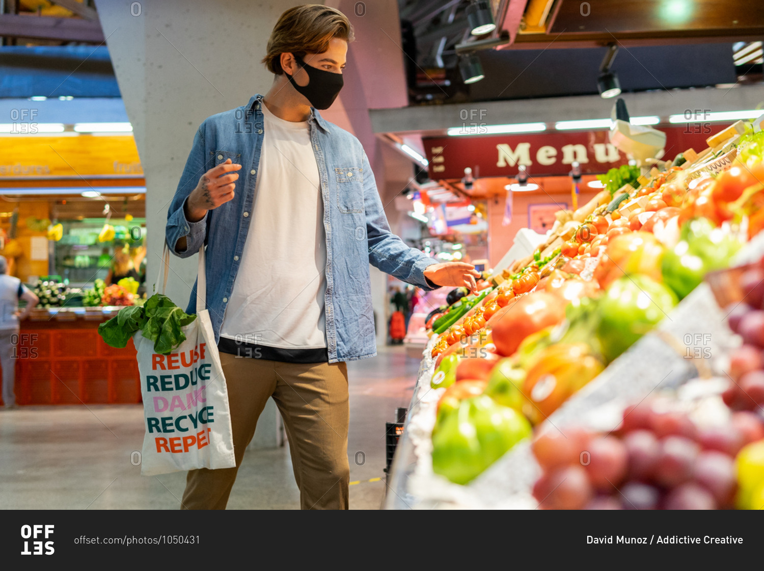 Young male customer in protective mask carrying eco friendly recycled fabric shopping bag and choosing fresh groceries while buying food in supermarket