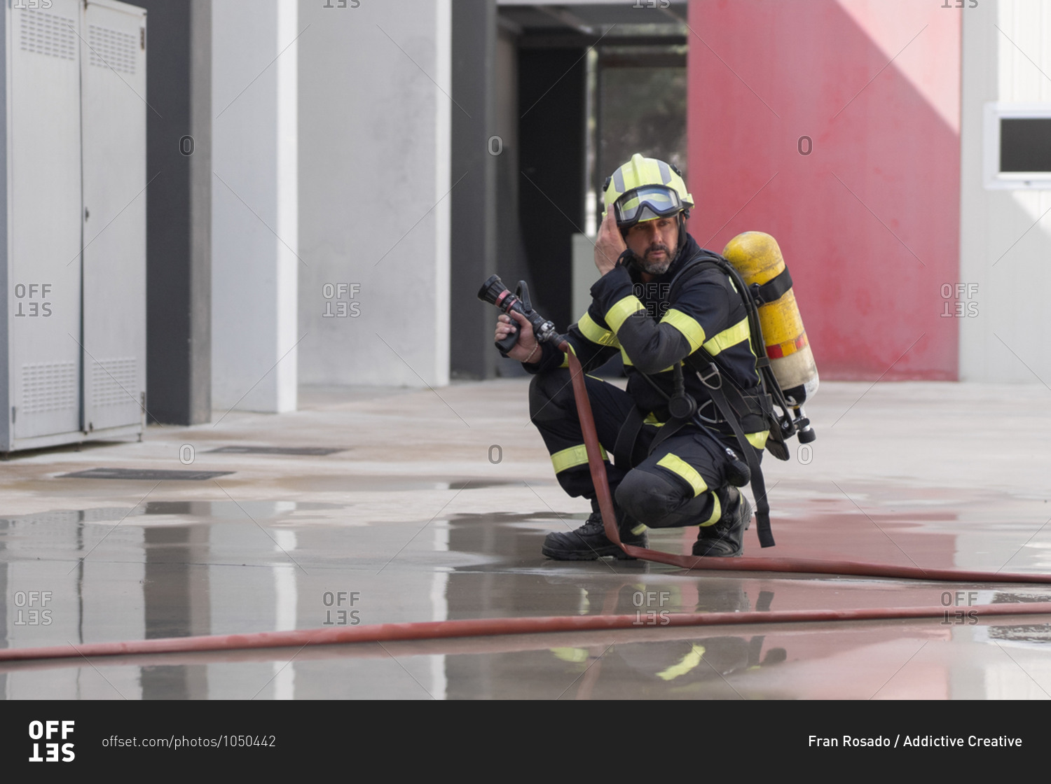 Contemplative unshaven firefighter in uniform with stripes and protective helmet reflecting in cement surface near hose at work while looking away