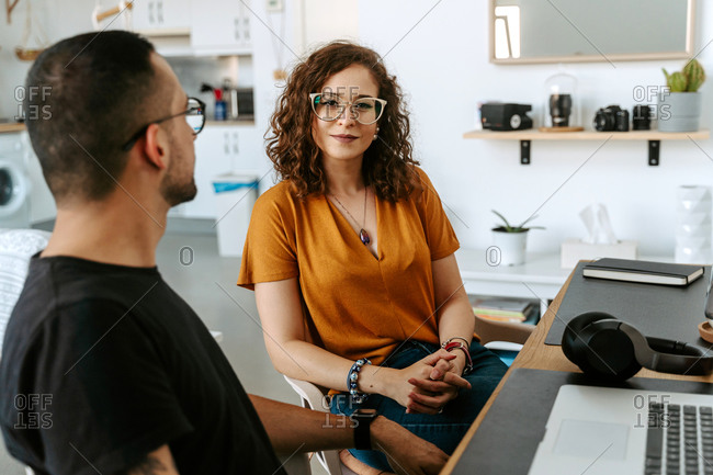 Side view of young bearded ethnic man and curly haired woman in casual clothes and eyeglasses working together on laptop during remote job at home