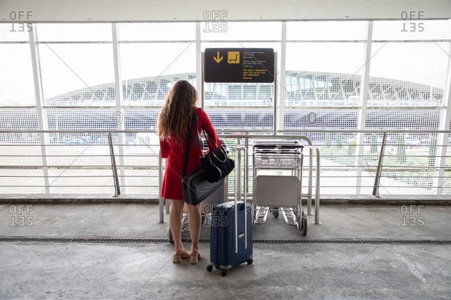 Back view of traveling female in airport collecting a baggage trolley and waiting for flight