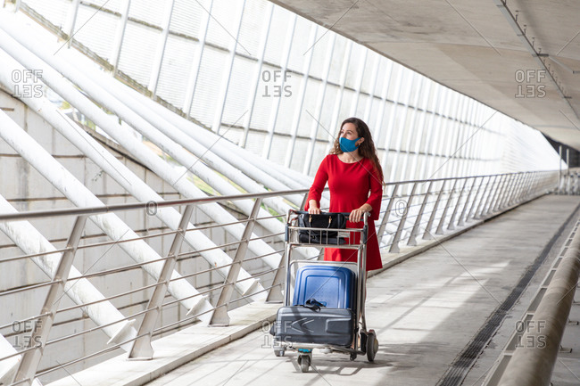 Traveling female walking in airport with baggage trolley and waiting for flight