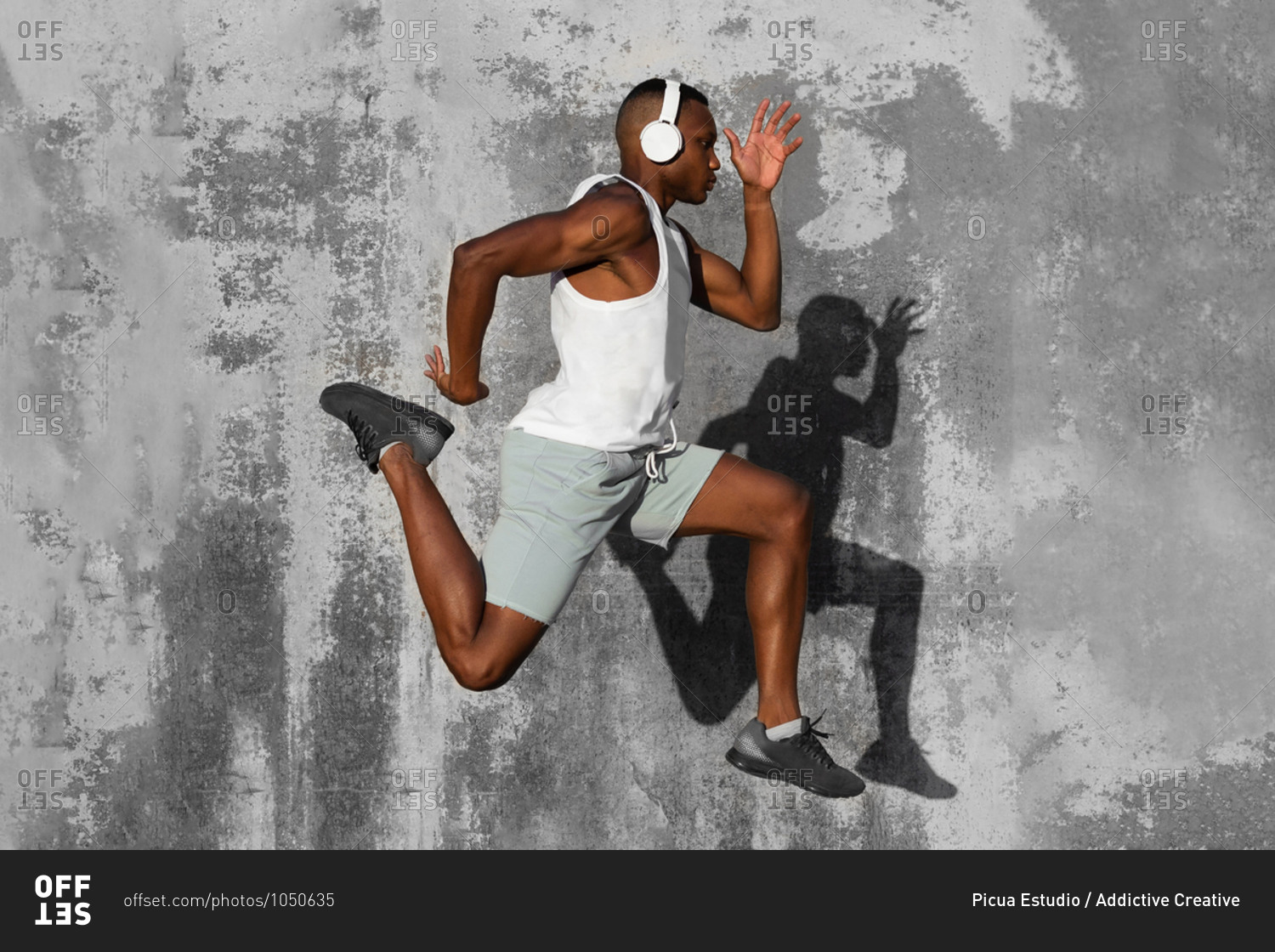 Full body side view of concentrated African American runner listening to music in headphones while jumping above ground during jogging training