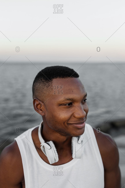 Positive cheerful ethnic male enjoying evening on shore of sea and looking away