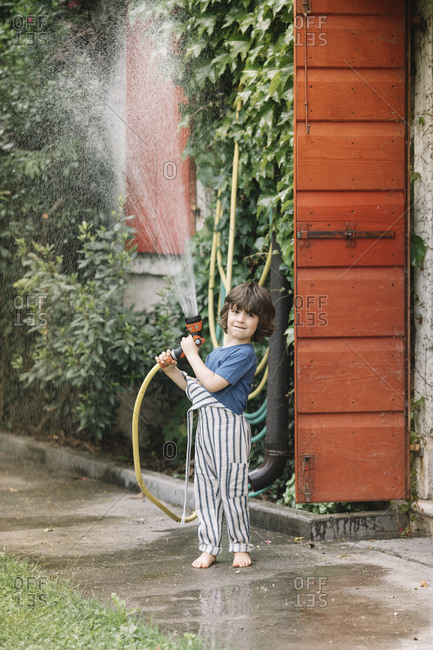 Boy playing with garden hose while standing at backyard