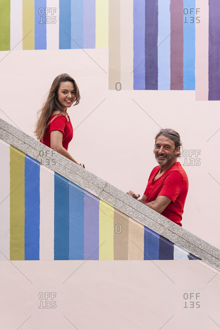 Smiling father and daughter standing on colorful staircase during sunny day