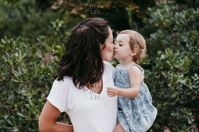 Happy mother and daughter kissing each other while standing in park