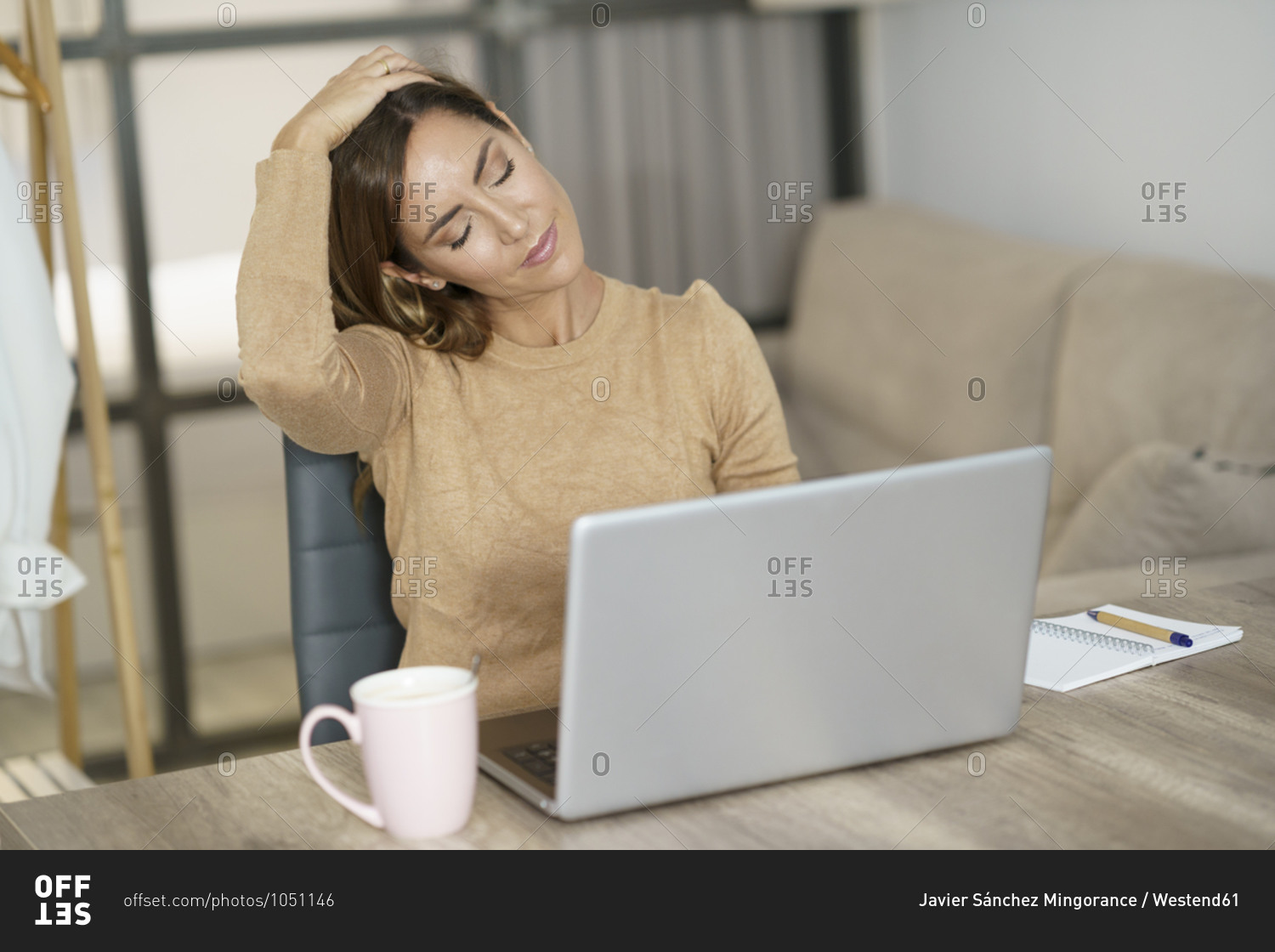 Businesswoman doing neck exercise while working on laptop at home