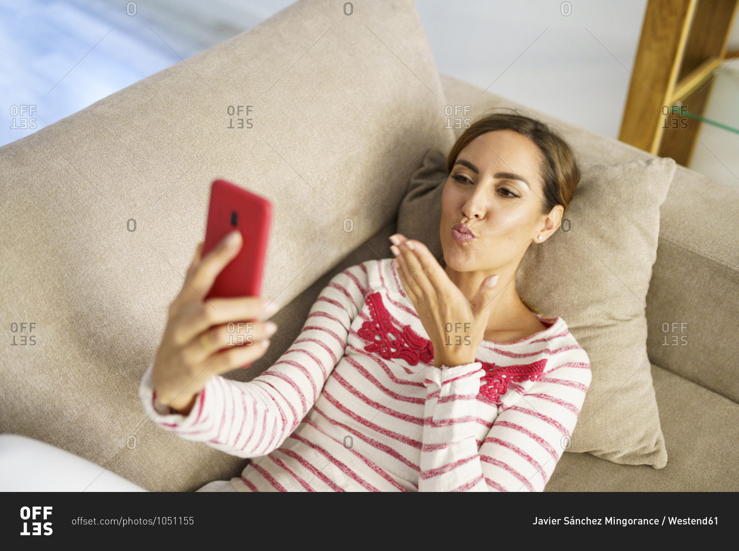 Woman giving kiss on video call while lying on sofa at home