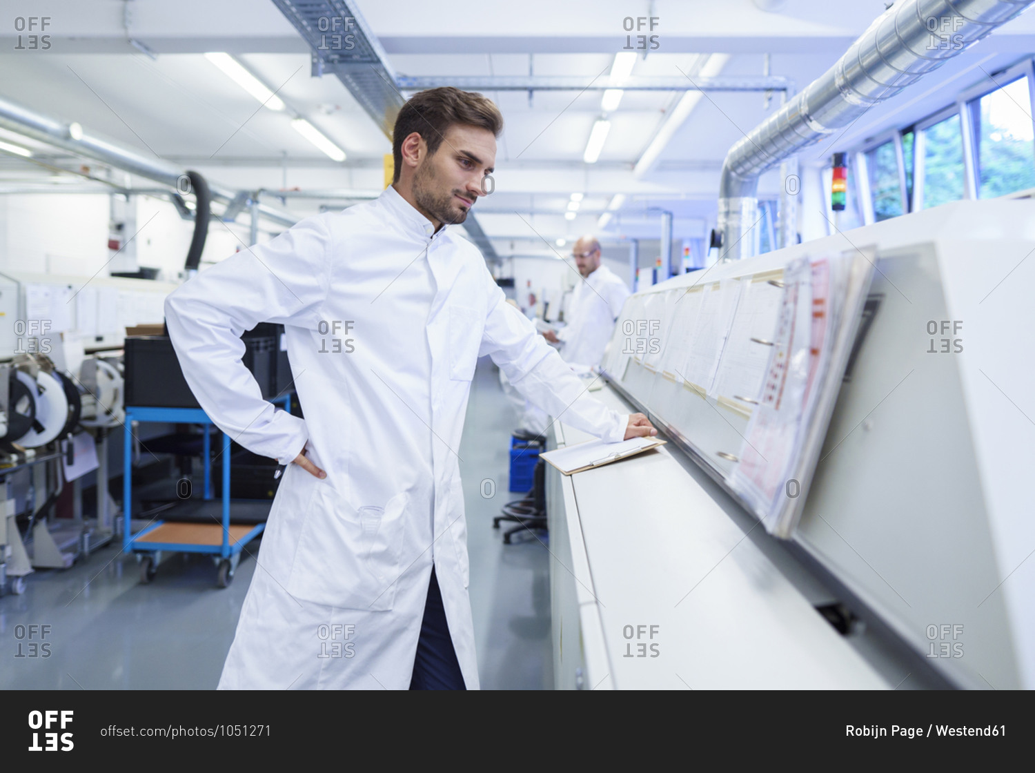 Young male technician in lab coat looking at reports on machinery
