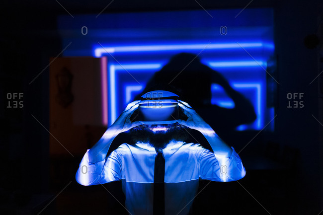Man holding virtual glasses while standing in blue light reflection at home during pandemic