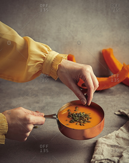 Woman chef sprinkles pumpkin soup with seeds