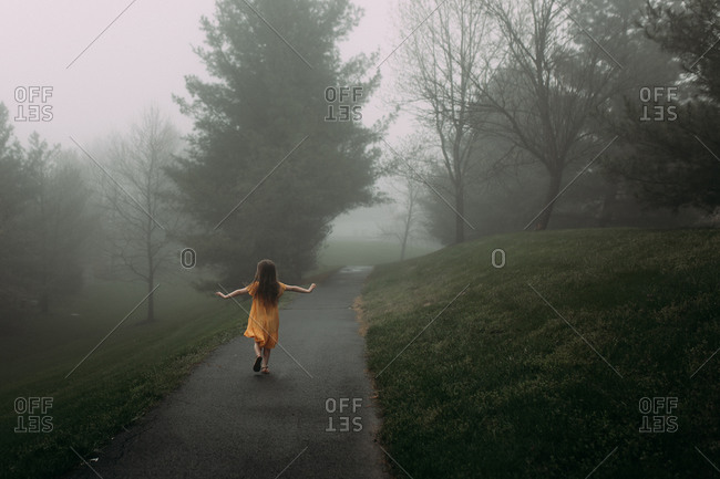 Young girl walking down a foggy path in a park