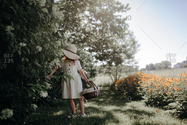 Young girl walking in a summer field with flowers wearing a white sun hat and matching dress