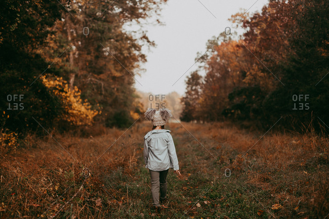 Back view of a little girl walking through a cleaning in an autumn forest