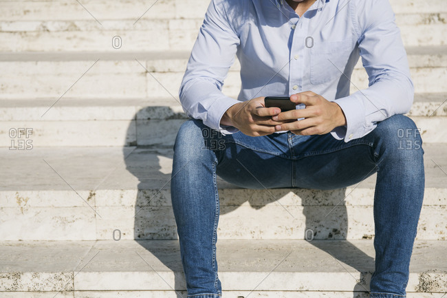 Man surfing internet through smart phone while sitting on steps during sunny day