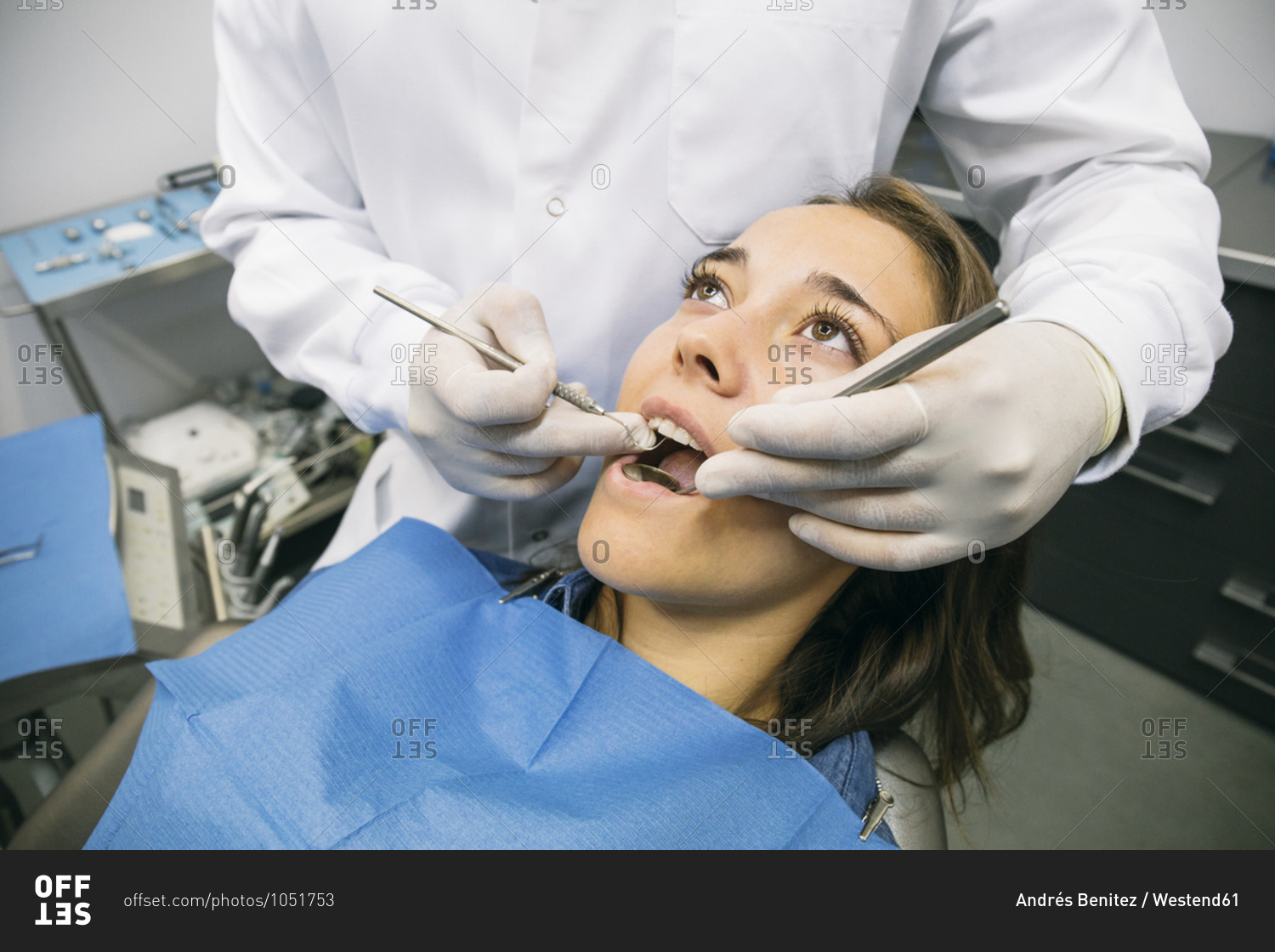 Male dentist in gloves examining oral cavity of pretty female patient at clinic