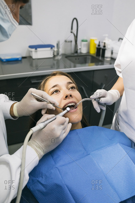 Male dentist doing dental treatment of female patient with help of assistant at clinic