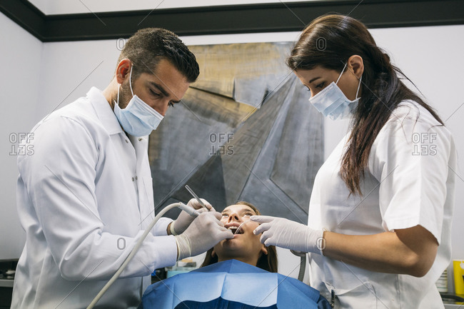 Male dentist in surgical glove and mask doing dental treatment of patient with help of female assistant