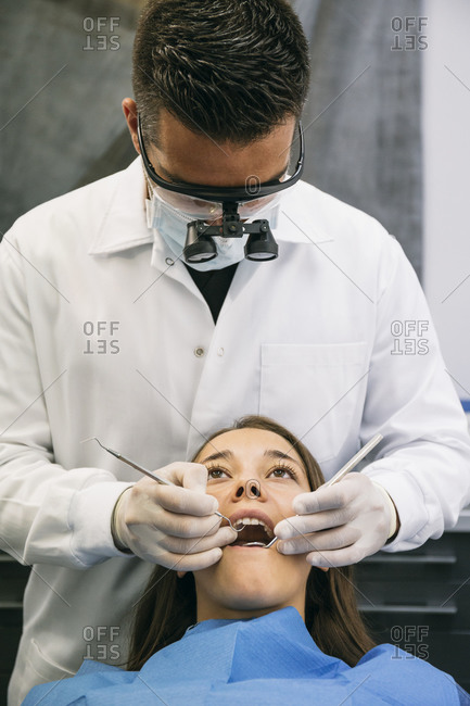 Male dentist wearing surgical loupes while examining teeth of young female patient in clinic