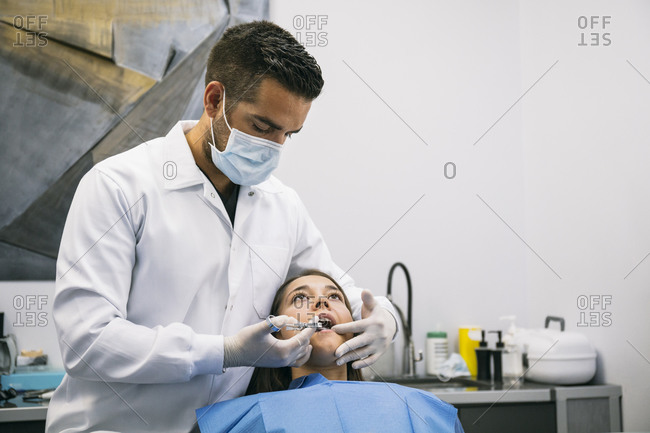 Male dentist anesthetizing young female patient before dental treatment at clinic