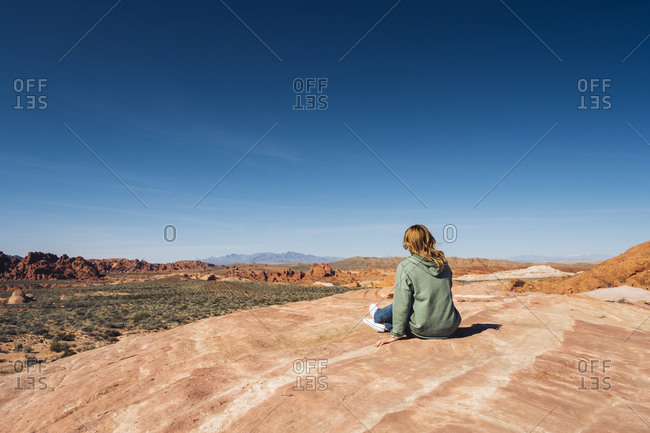 Woman sitting on rock formation at Valley of Fire State Park against blue sky- Nevada- USA