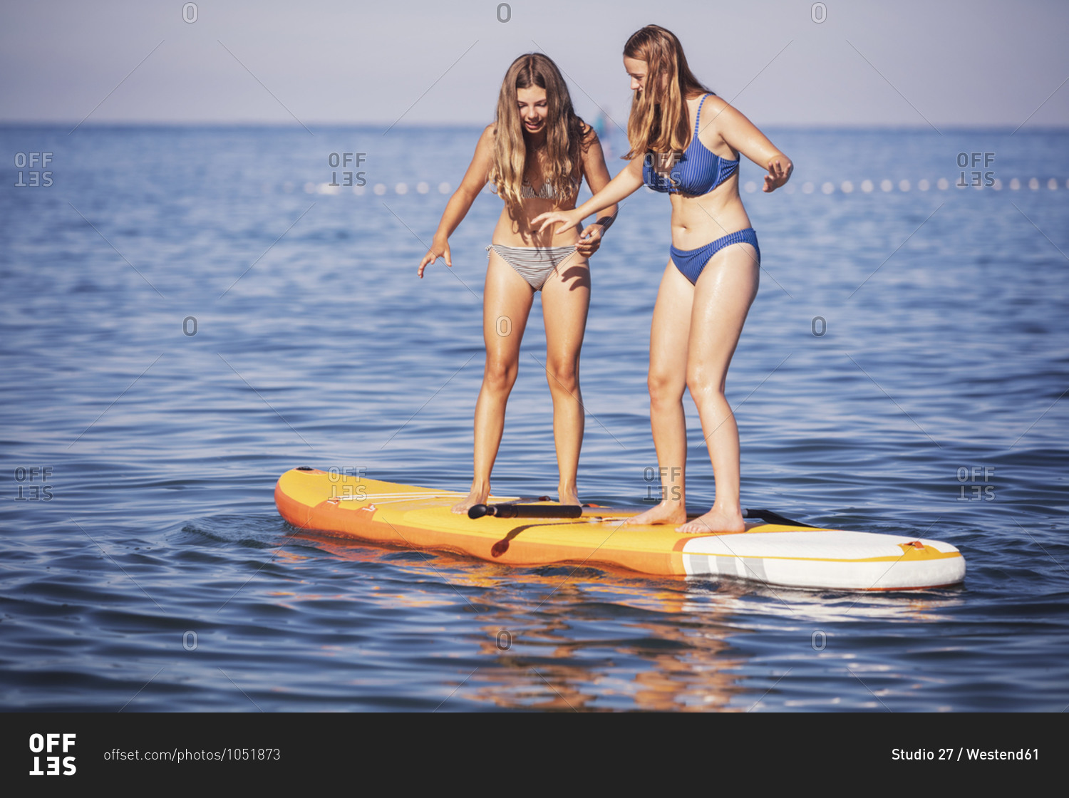 Friends Standing On Stand Up Paddle Board In Sea During Sunny Day Stock Photo Offset