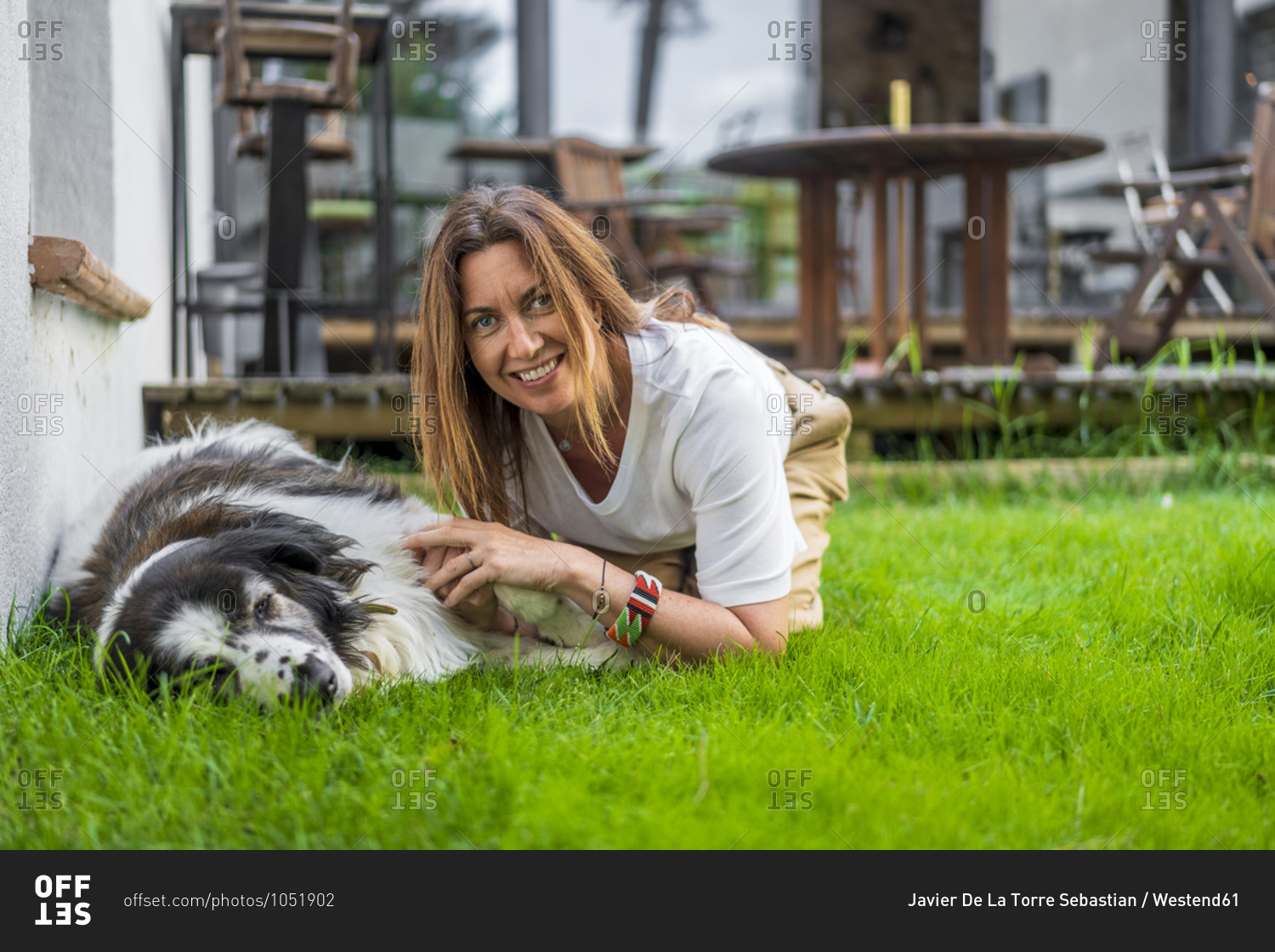 Happy woman kneeling by dog relaxing on grass at back yard