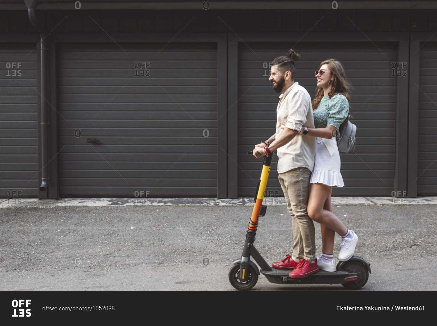 Smiling couple riding electric push scooter on street in city