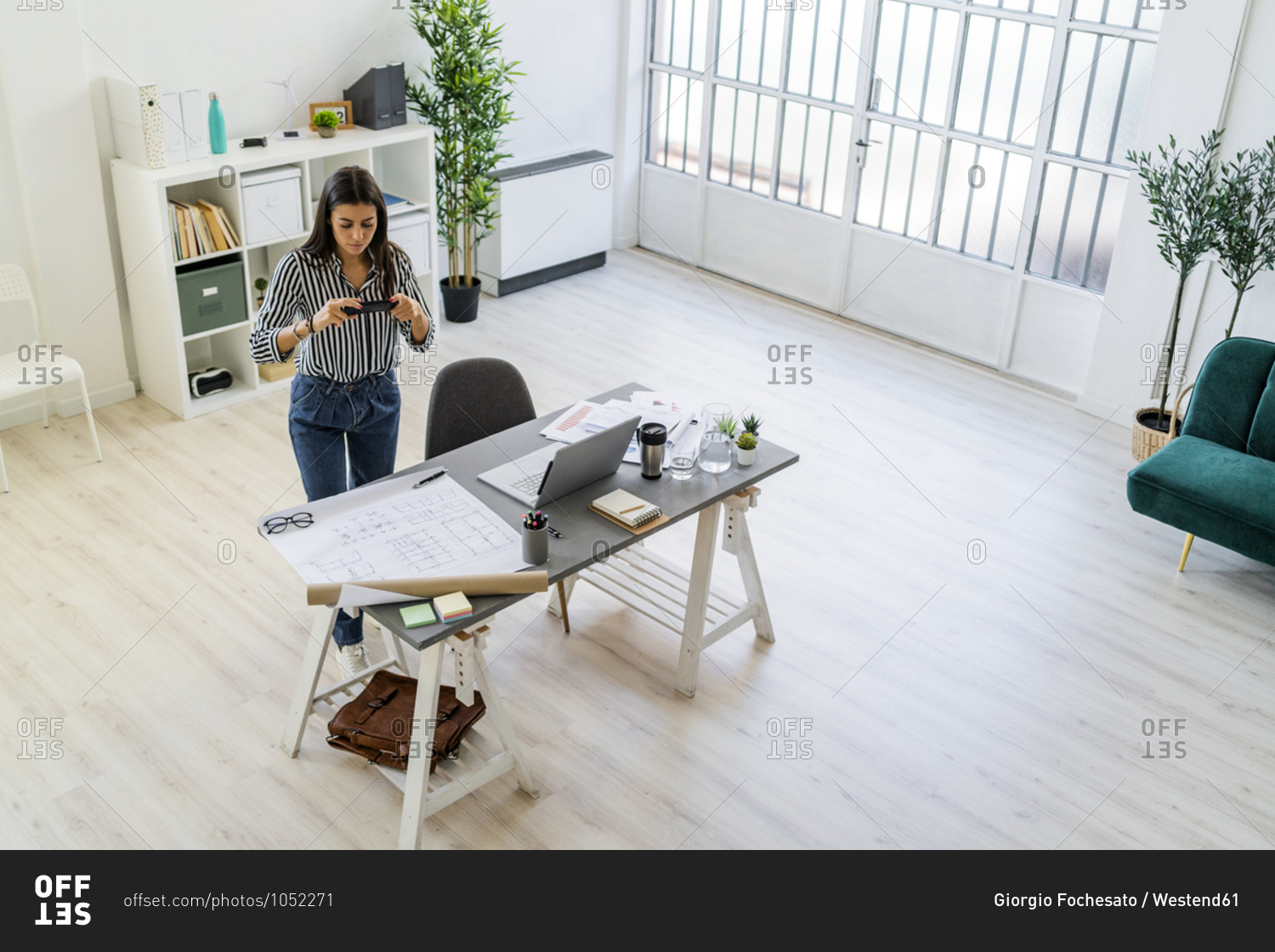 Female architect photographing blueprint at desk in creative workplace