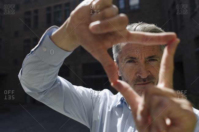 Businessman looking through finger frame while standing against building