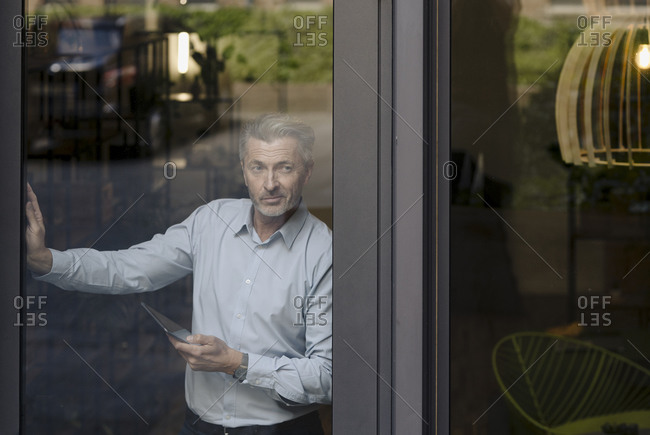 Businessman using digital tablet while standing by glass wall at office