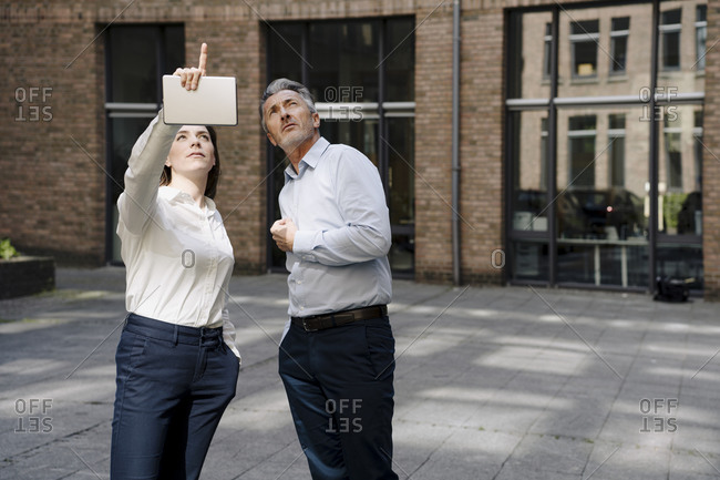 Businesswoman pointing up while standing by man against building