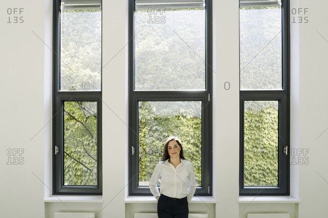 Businesswoman with hands behind back standing against window at office