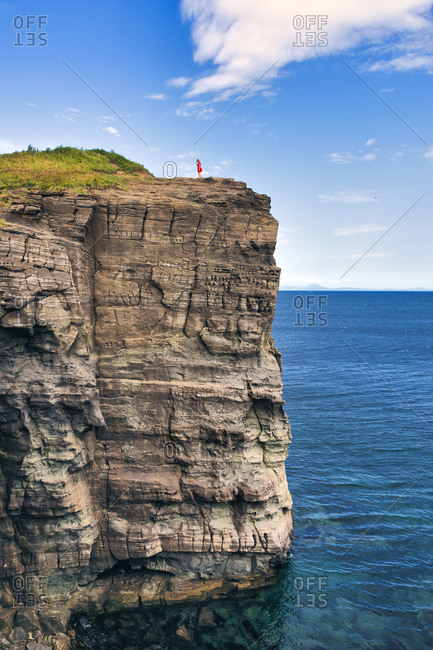 Distant view of woman standing on cliff by sea against sky