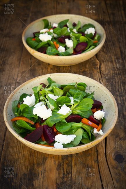Two bowls of vegetarian salad with roasted carrot strips- beetroot- corn salad- goat cheese and Spanish onions