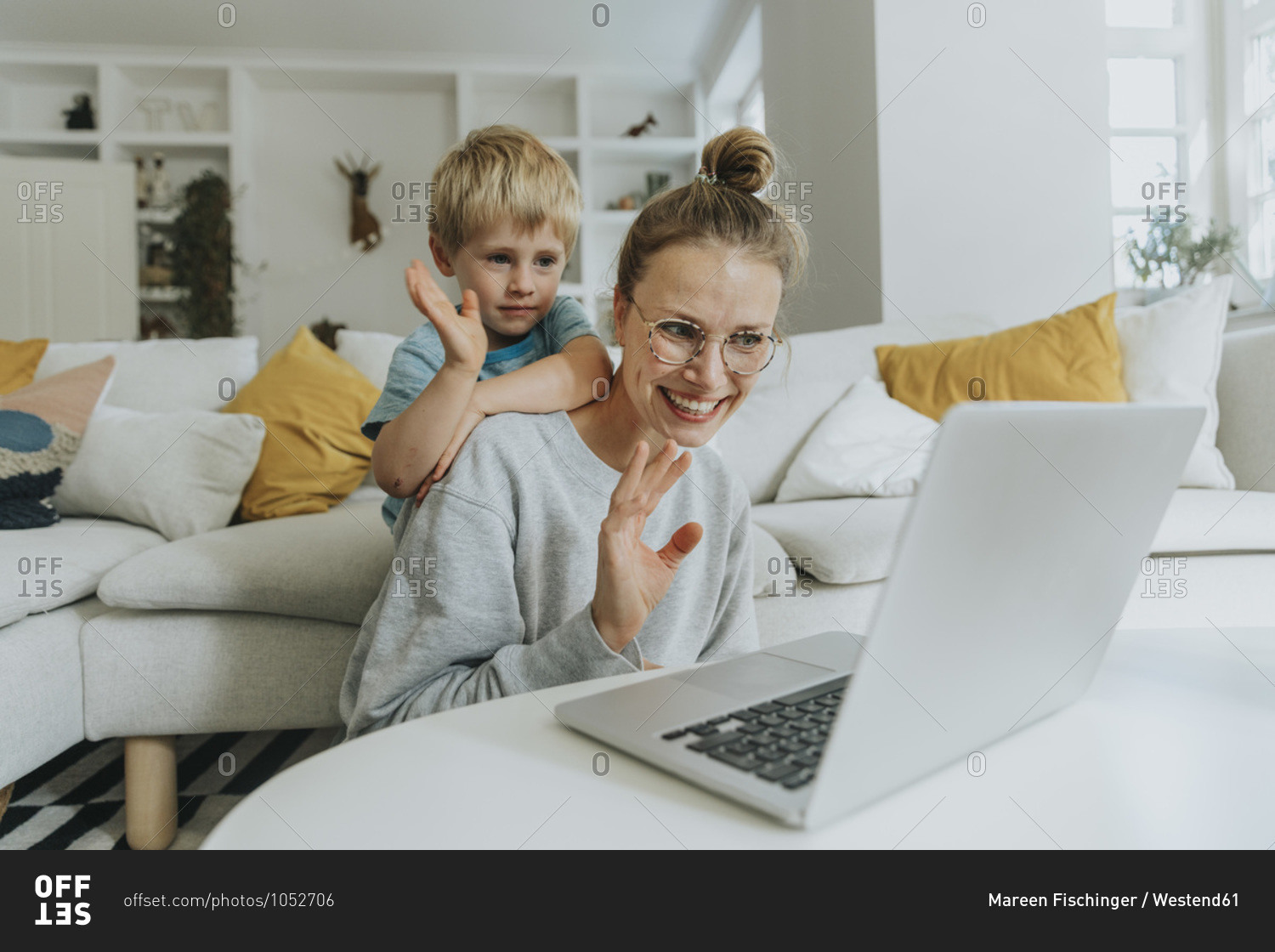 Mother and son waving hand to video call on laptop while sitting at home