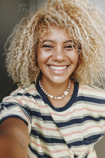 Happy Hispanic woman with blond curly hair taking selfie